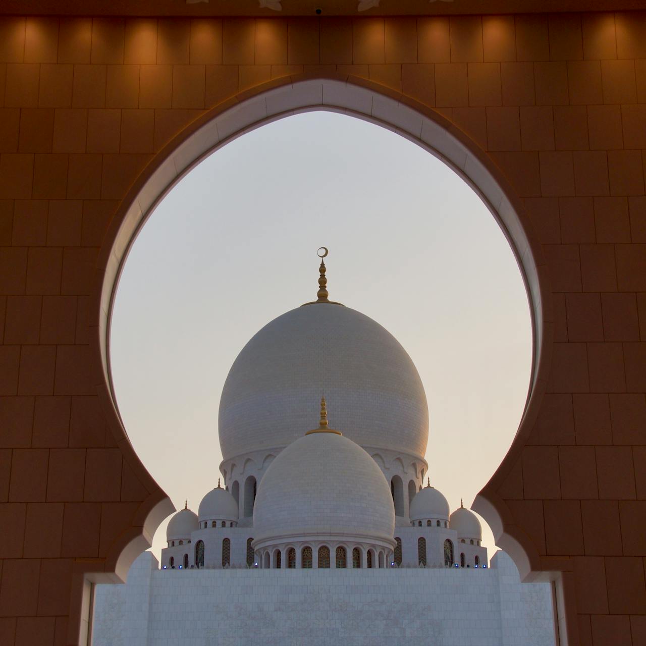 A captivating view of the Sheikh Zayed Grand Mosque's dome framed by an ornate arch in Abu Dhabi.